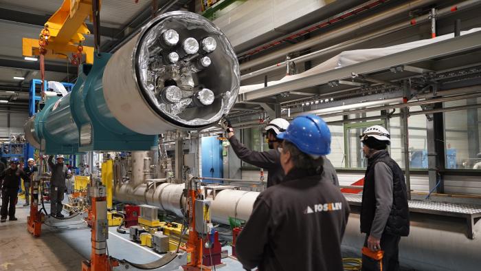 magnet carried by crane with engineers in hard hats looking at it